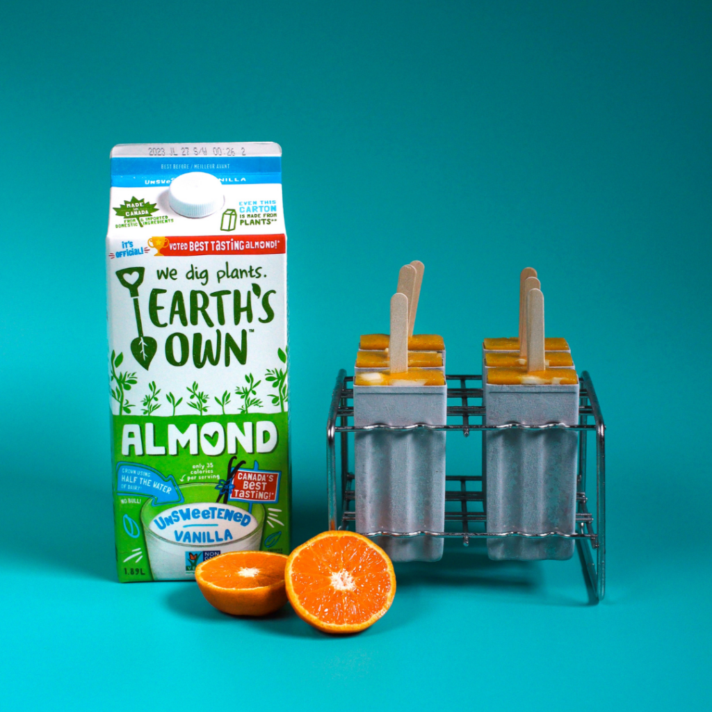 Orange Creamiscle Popsicles placed beside almond milk carton with a blue background